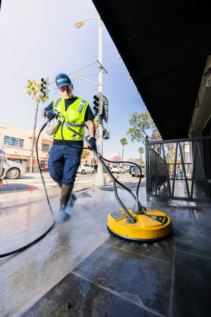 A crew member in a hi-vis vest pressure washing a commercial sidewalk