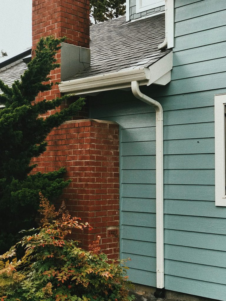 A blue sided house with a red brick chimney and clean gutters after exterior washing