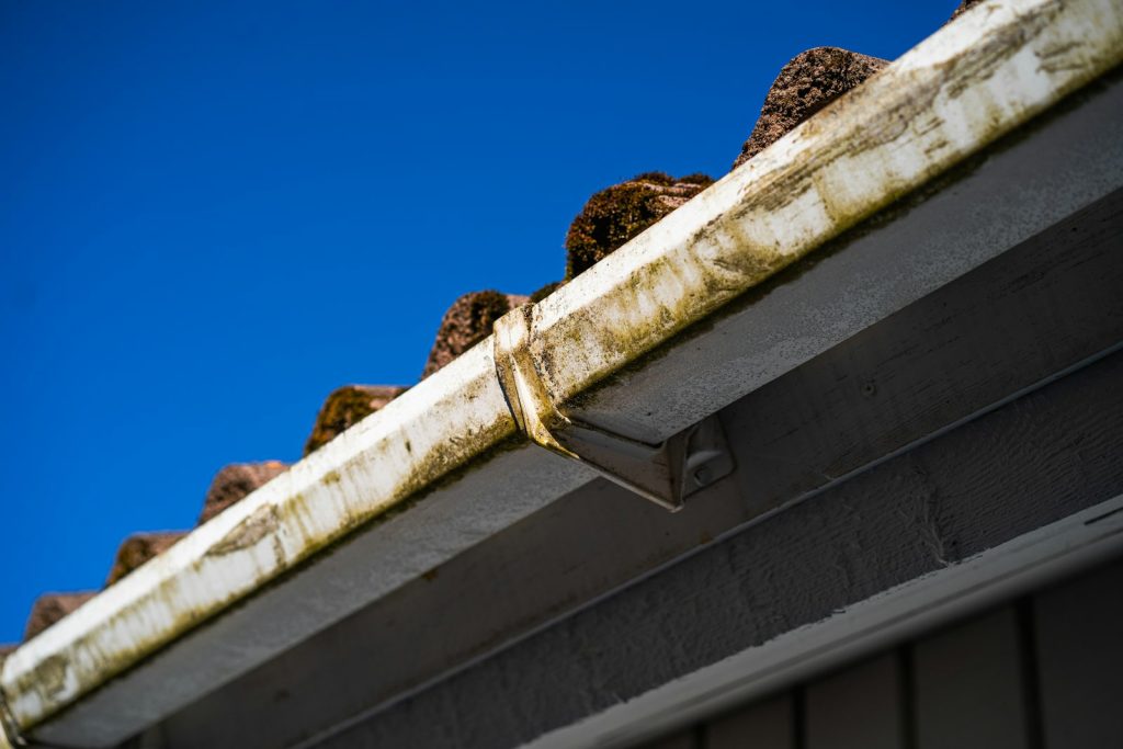 Debris-filled gutters along a roofline against a blue sky before gutter cleaning